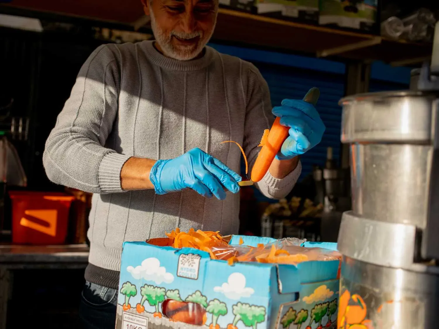 Un préparateur en gants bleus épluche des carottes au-dessus d'une caisse