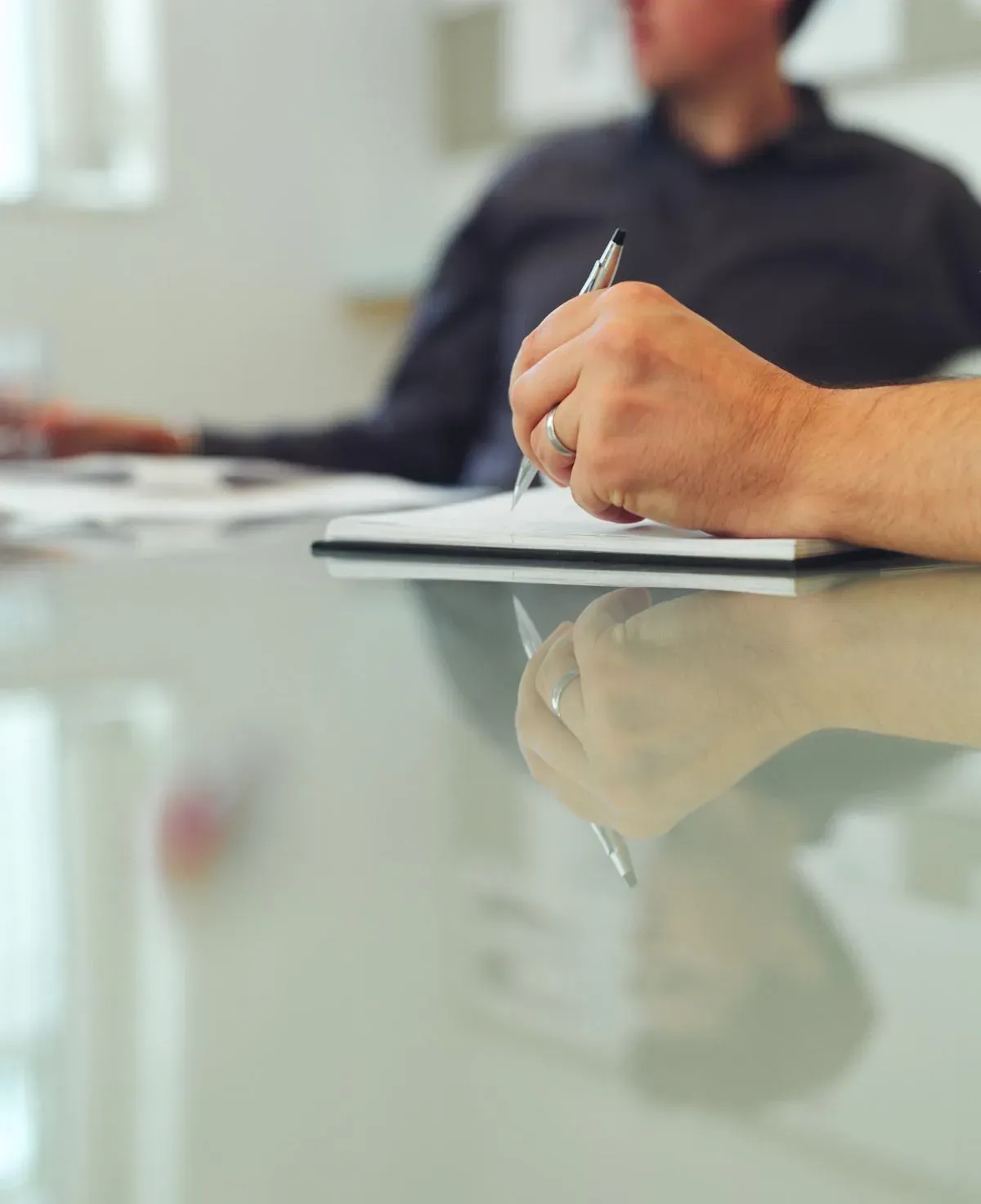 Une main remplit un formulaire papier posé sur un bureau en verre