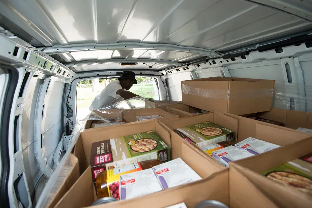Des cartons de denrées rangés dans une camionnette, qu’un homme ajuste depuis la porte arrière