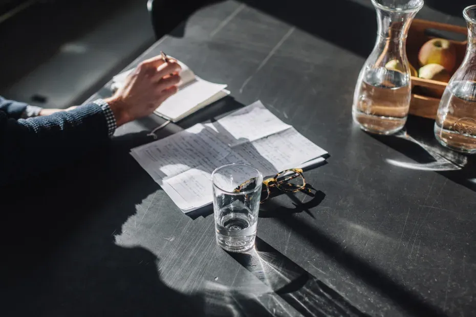 Des factures et des notes posées sur une table sombre, à côté d'un verre d'eau
