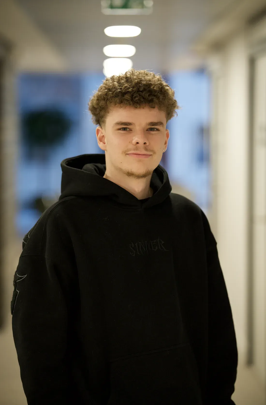Enzo Delamarre, sweat à capuche noir, dans un couloir lumineux