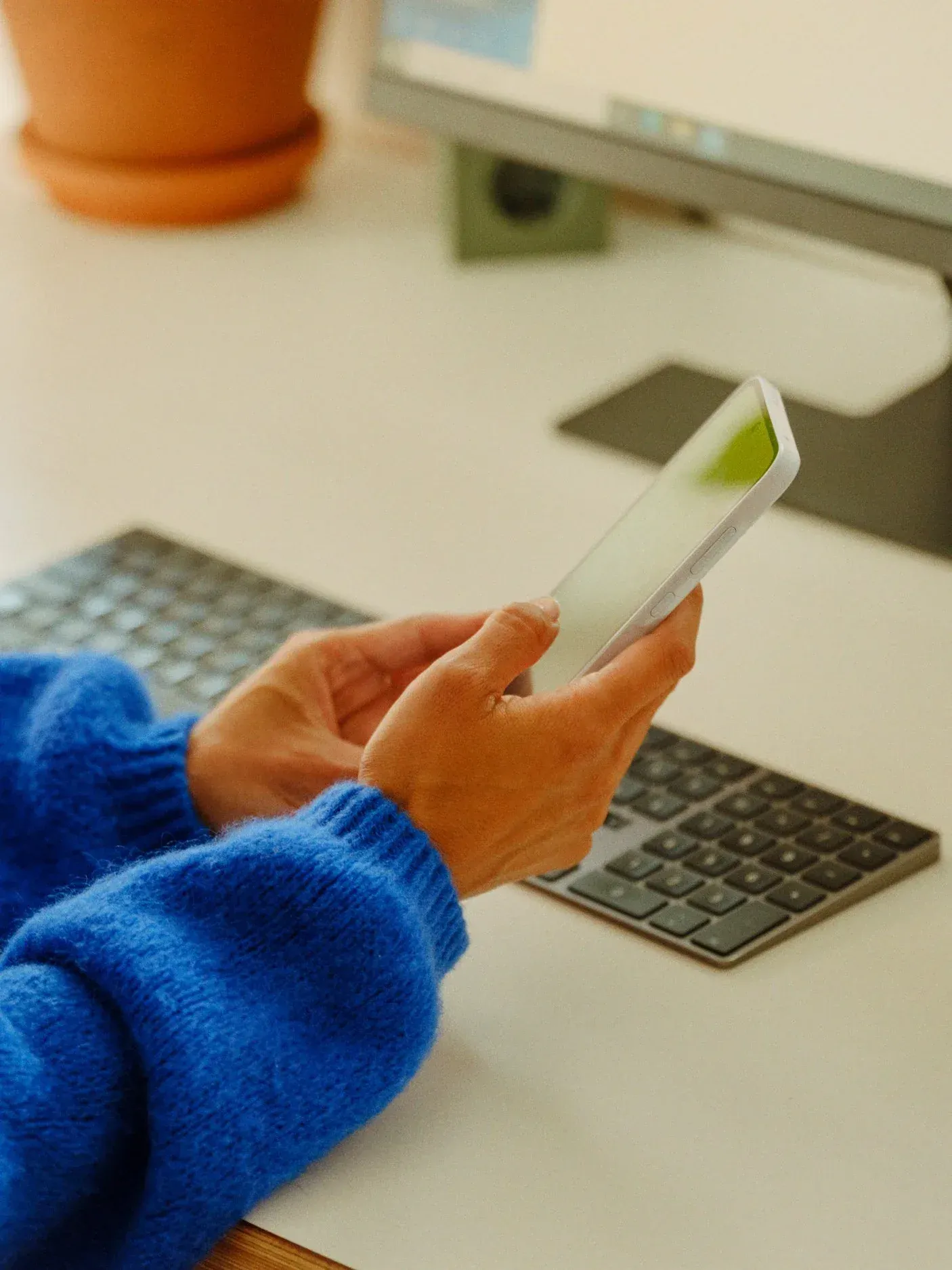 Mains tenant un téléphone devant un clavier, sur un bureau