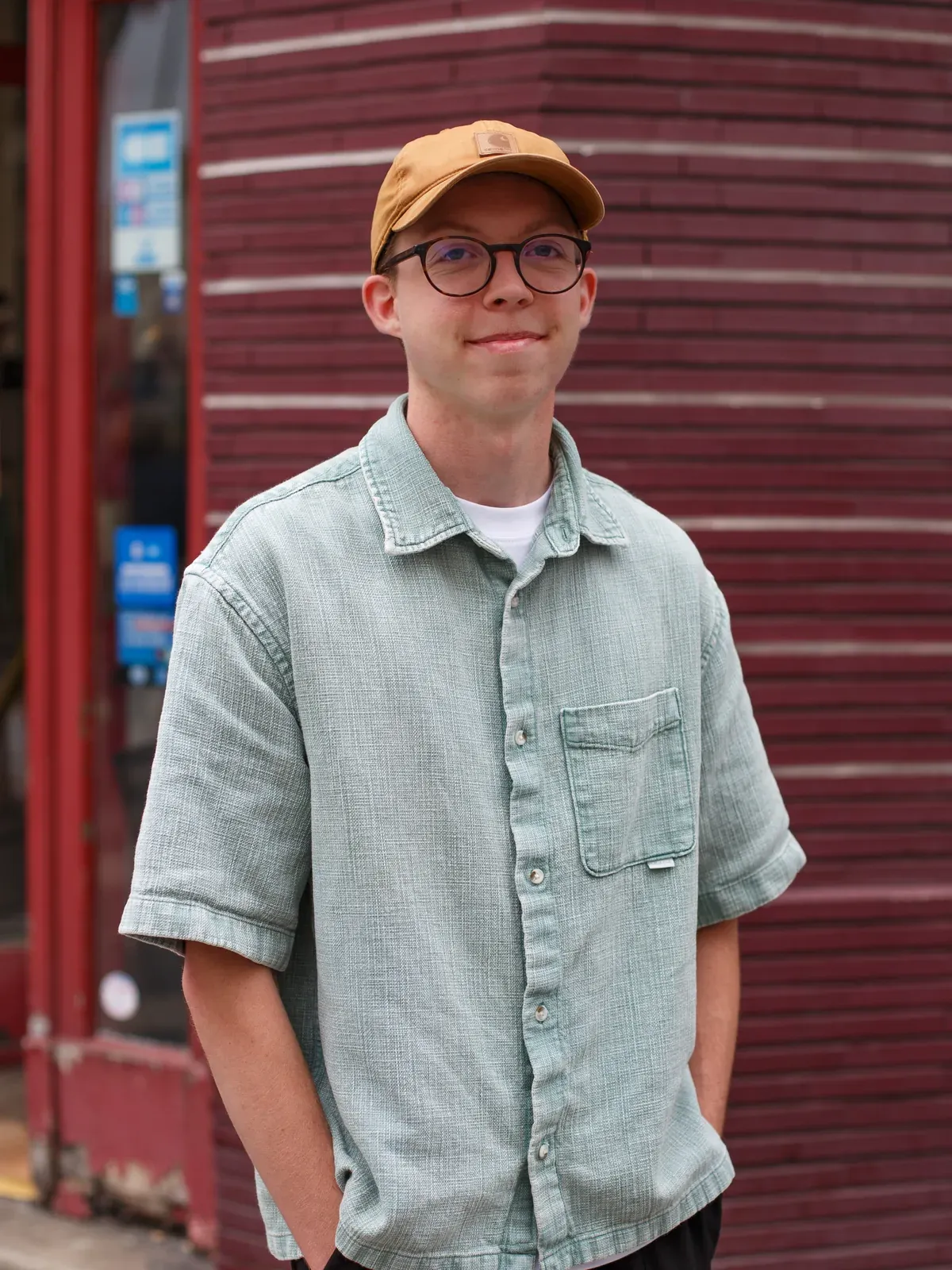 Louis Prochwicz, casquette et chemise en jean, devant un mur de briques rouges